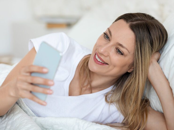 Frau im Bett mit Handy in der Hand