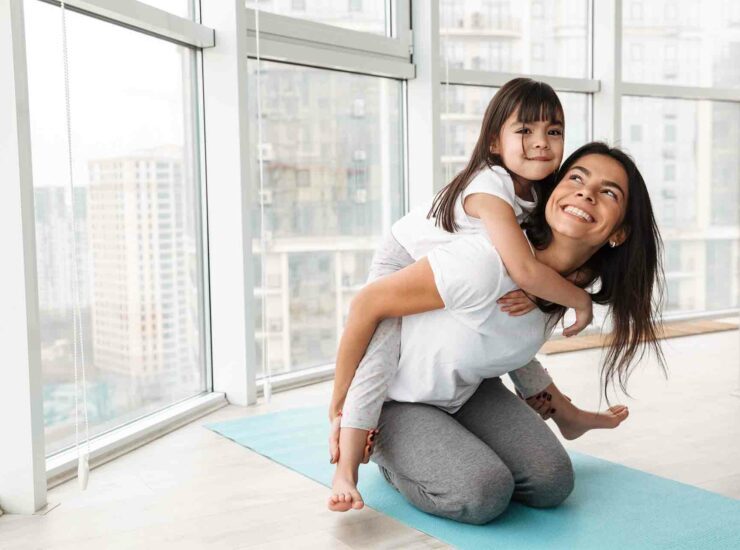 Mutter auf Yogamatte mit Tochter auf dem Rücken