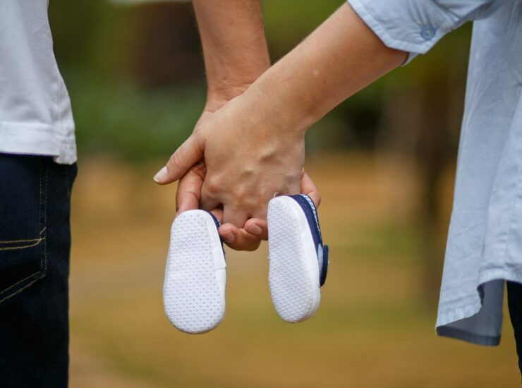 Paar hält Händchen und hat Babyschuhe in den Händen